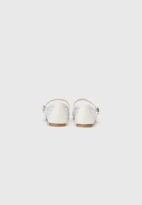 Ballerines blanches avec une lanière, présentant un design tissé texturé sur les côtés et un petit talon. Fini en cuir lisse et semelle en bois.