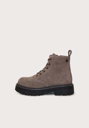 Bottine en daim marron avec semelle noire épaisse, lacets à l'avant et languette à l'arrière sur fond blanc.