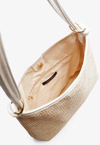 Beżowa torba tote o splocie z teksturowanym wykończeniem ze słomy, gładkim białym wnętrzem i zamykaną na zamek kieszonką, z złotymi akcentami i podwójnymi uchwytami.