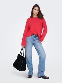 Pull rouge oversize à manches longues, associé à un jean évasé bleu clair. Sac cabas en daim noir et bottines à talons noires complètent la tenue.