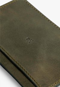 Cartera de cuero verde con costuras visibles, logotipo de calavera en relieve y una textura suave. El detalle de los bordes añade sofisticación al diseño.