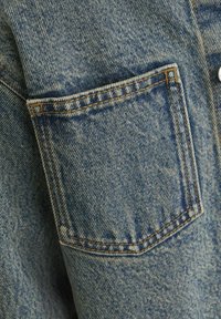 Jeansjacka i blått tyg med en bröstficka, kontrasterande stickningar och en lätt blekt yta.