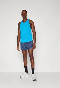 Vyriška mėlyna sportinė liemenė su apvalia iškirpte, derinama su raštuotais tamsiai mėlynais šortais. Avimi balti sportiniai bateliai ir juodos kojinės.