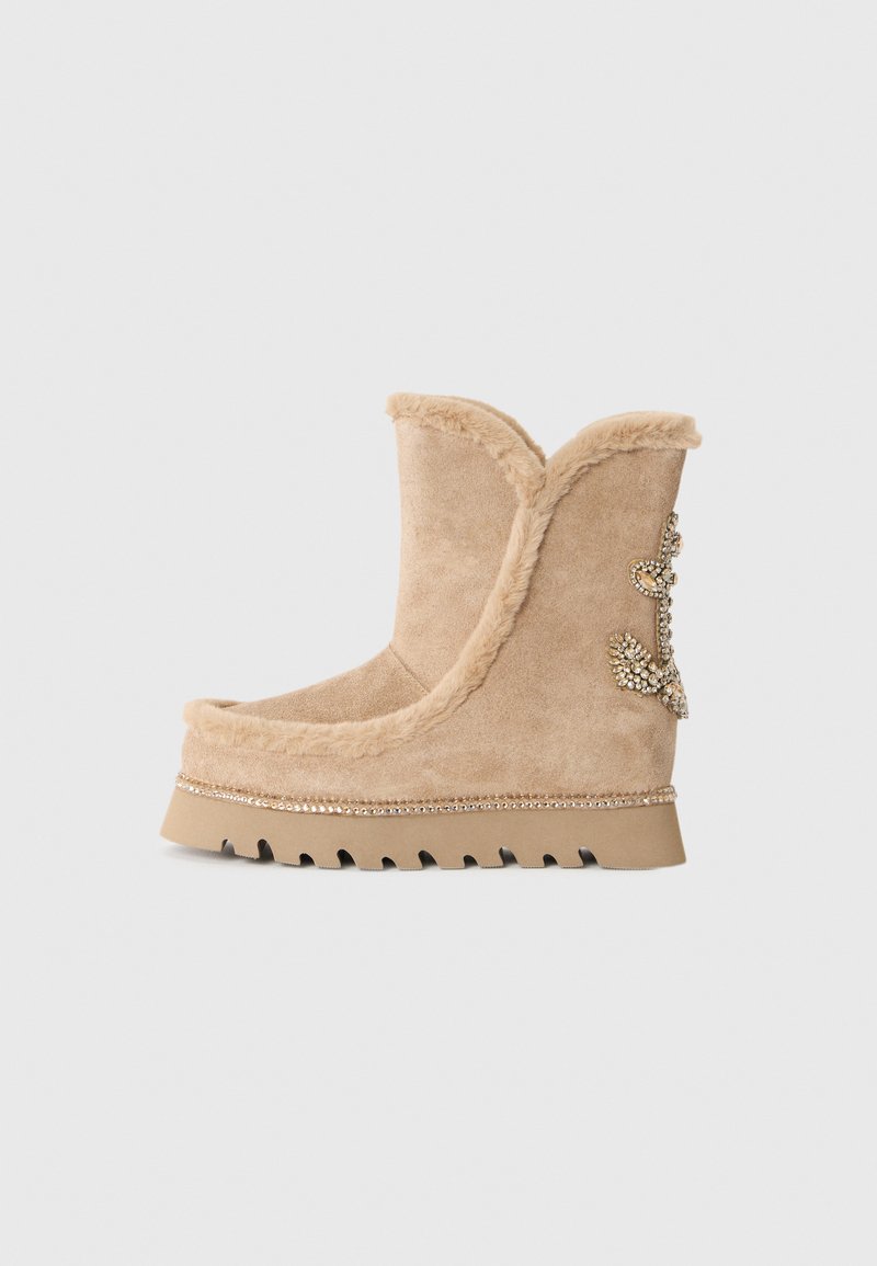 Bottes de cheville en suède beige avec garniture en fourrure synthétique, accents décoratifs en strass et semelle en caoutchouc striée. Présente un bout rond et un dessus incurvé.