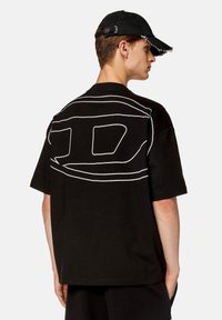 T-shirt nera oversize con un design astratto bianco sul retro. Realizzata in cotone, presenta maniche corte e scollo rotondo.