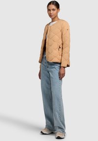 Giacca imbottita beige con colletto rotondo, tasche con zip e polsini a costine. Abbinata a jeans a gamba dritta di colore azzurro chiaro e sneakers beige.