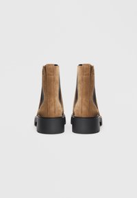 Brown suede ankle boots with black elastic side panels, featuring a rounded toe and thick black rubber sole. Simple, sleek design.