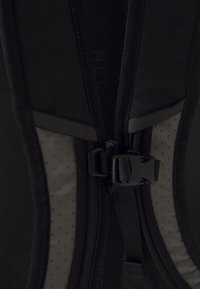 Gros plan d'une sangle de poitrine noire de sac à dos avec une boucle en plastique et des bretelles rembourrées avec des panneaux en mesh respirant.