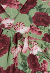 Kwiatowa sukienka z zielonym tłem, ozdobiona różowymi i burgundowymi piwoniami, z plisowanym pasem i metalicznym logo. Miękka faktura materiału.