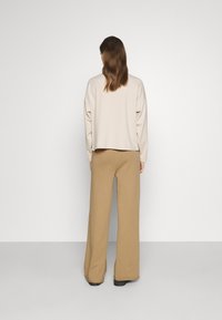 Sweatshirt beige court avec des épaules tombantes et une coupe ample, associé à un pantalon tan taille haute et large. Texture de tissu lisse.