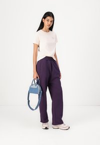 Ljusrosa bomullströja, avslappnad passform; mörklila högmidjade byxor; liten blå denimhandväska med korta handtag; avslappnade sneakers.