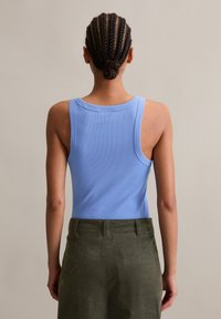 Blaues ärmelloses Tanktop mit geripptem Textur, Rundhals und breiten Trägern, kombiniert mit olivgrünen Hosen.