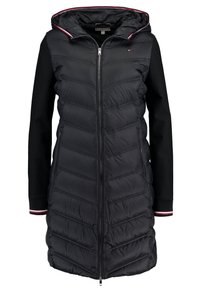 Zwart pufferjack met een ritssluiting aan de voorkant, geborduurd ontwerp en een capuchon. Heeft contrasterende zwarte mouwen en een gestreepte accentuering op de voering van de capuchon.