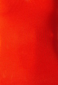 Tissu rouge côtelé avec des rayures verticales, une texture lisse et une coupe ajustée, mettant en valeur son élasticité et ses lignes structurées.