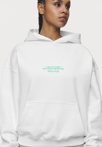 Bílá mikina s kapucí, přední kapsou a stahovací šňůrkou, s tyrkysovým vyšitým textem: "FOCUS IN THE GOOD PEGADOR." Měkká tkanina z bavlněného směsového materiálu.