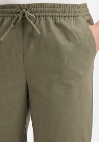 Leichte, olivgrüne Baumwollmischungshosen mit elastischem Bund, Kordelzug und Seitentaschen. Schlichtes Design mit strukturierter Oberfläche.