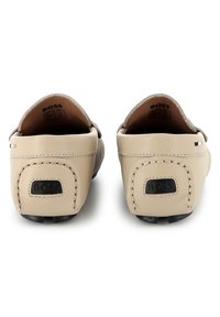 Beige ādas loafers ar gludu tekstūru, noapaļotu aizmuguri un melnu logo detaļu; satur izšūtu akcentu un strukturētu melnu zoli.