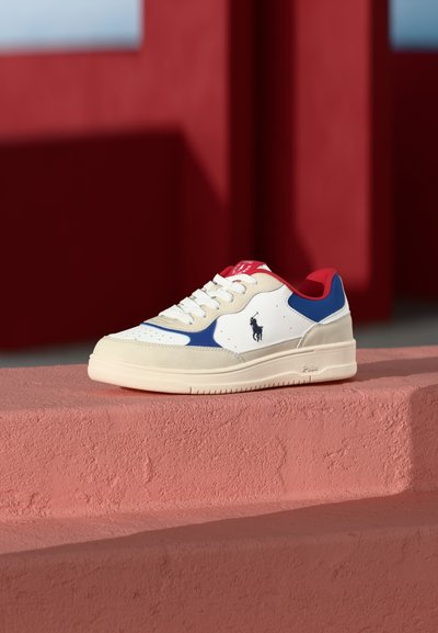 Bílé tenisky s modrými a červenými akcenty, hladká kůže a semišové materiály, kulatá špička, tkaničky a logo na boku.