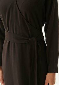Schwarzes Wickelkleid mit langen Ärmeln, ausgestattet mit einem gebundenen Gürtel in der Taille. Glatter Stoff mit weicher Textur und ohne sichtbare Muster oder Beschläge.