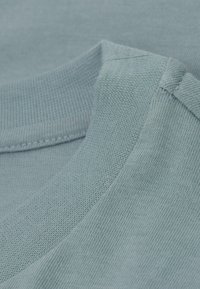 Světle modrá bavlněná látka s hladkou texturou, se zaobleným výstřihem a detailním pohledem na švy a žebrování.