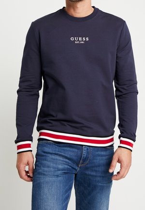 Sweatshirt bleu marine en tissu doux, avec un col rond, des poignets et un ourlet côtelés rayés rouge et blanc, et un texte logo à l'avant.