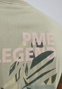 Hellgrünes Baumwoll-T-Shirt mit pinkem Text "PME LEGEND" und einem tropischen Blattdruck in Dunkel- und Hellgrün auf dem Rücken.