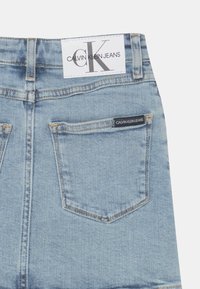 Jeans Calvin Klein em denim azul claro; apresenta um rótulo branco na cintura com o nome da marca e uma pequena etiqueta preta na parte de trás do bolso.