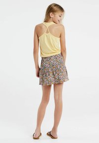 Top giallo senza maniche con design a racerback abbinato a una gonna con motivo floreale in tonalità di rosa, giallo e verde. Sandali piatti.