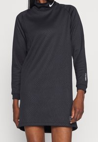 Musta pitkähihaisista mekko korkealla kauluksella, tekstuuripinta-aallot ja Nike-logo hihassa. Valmistettu pehmeästä ja joustavasta kankaasta.