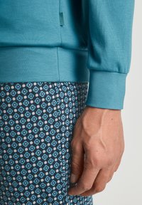 Blauwe crewneck sweatshirt met een textuur stof. Geprinte donkere broek toont kleine blauwe en witte bloemmotieven.