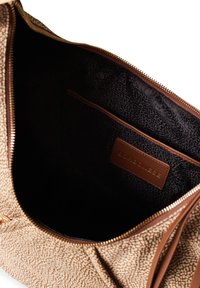 Brown patterned tote bag with a zipper closure. Interior features a dark lining and a small leather pocket with the brand name embossed.