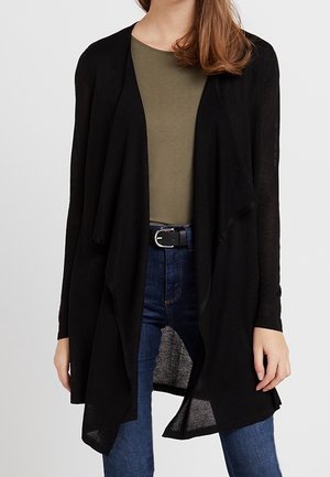 Cárdigan negro ligero con un diseño de frente abierto. Presenta mangas largas y un ajuste relajado, usado sobre una blusa verde oscura y jeans azules.