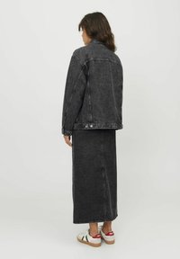 Zwart denim jack met bijpassende lange rok. Beide items hebben een klassieke snit en een gladde textuur, aangevuld met witte sneakers.