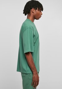 Tricou din bumbac verde, cu o croială lejeră și mâneci scurte, având un gât rotund și detalii subtile cu slit lateral, asortat cu pantaloni matching.