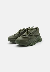 Zapatillas de deporte verdes de malla y goma con un diseño voluminoso, que presentan paneles texturizados, suelas gruesas y cierre con cordones.