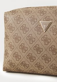 Brown synthetic bag featuring a diamond pattern, embossed logo, and triangular metallic hardware. Smooth texture with subtle accents.