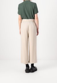 Light beige, wide-leg trousers with an elastic waistband, paired with a dark green short-sleeve top and black platform shoes.
