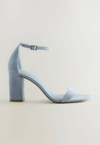 Sandale à talon bloc en daim bleu clair avec bride à la cheville et bande avant à l'orteil, montrée de profil sur un fond neutre.