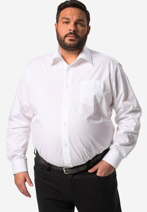 Bílá košile s dlouhým rukávem a zapínáním na knoflíky, která má náprsní kapsu a kontrastní manžety, doplněná tmavými kalhotami a černým opaskem.