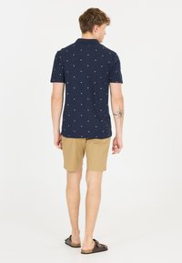 Marinblå polo-t-shirt med vitt mönster, korta ärmar och krage; kombinerad med beigefärgade shorts och bruna sandaler. Ren design och avslappnad passform.