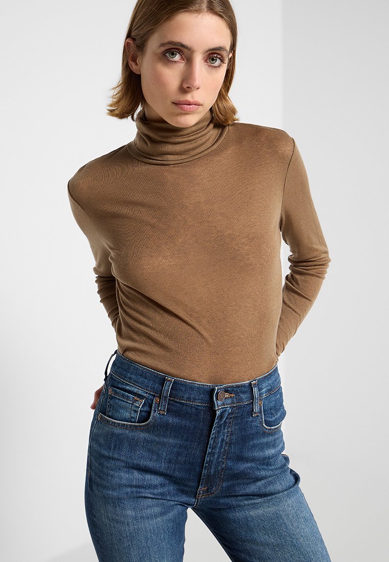 Maglione marrone a maniche lunghe con collo alto abbinato a jeans blu a vita alta. Il tessuto sembra liscio con un design aderente e una texture minimale.
