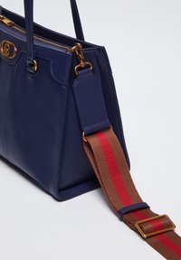 Borsa in pelle blu navy con hardware dorato, caratterizzata da una superficie testurizzata e una tracolla marrone removibile con righe rosse.