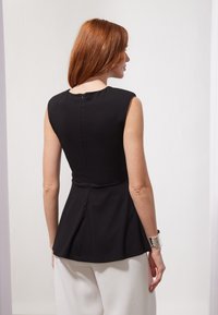 Svart peplum topp med korte ermer, med en tilpasset bodice og glidelås bak. Glatt stoff og definert silhuett med en utvidet kant.