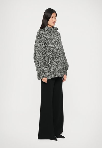 Gebreide zwart-wit gespetterde oversized sweater met een hoge kraag en brede mouwen, gecombineerd met zwarte wijde broekspijpen.