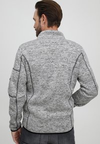 Grå, struktureret sweater med høj krave, kontrasterende syninger og rib strik ved håndleddene. Har en ensfarvet sort kant i bunden.