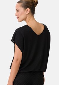 Top nero, dal taglio morbido e chic, con maniche corte e schiena a V. Tessuto soffice, materiale leggero e silhouette rilassata.