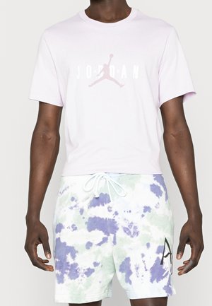 Homme portant un t-shirt Jordan rose clair et un short tie-dye blanc, violet et vert avec une taille à cordon.