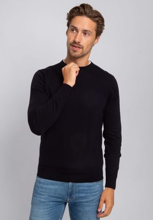 Black crew-neck sweater made of knit fabric, featuring long sleeves and a ribbed hem. Worn with light blue denim jeans.