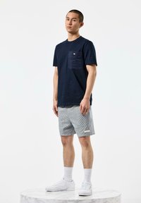 Navy crew neck t-shirt with a chest pocket, paired with gray and white striped shorts, and white sneakers. Set against a plain background.
