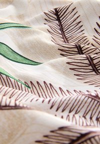 Tissu crème avec motifs de feuilles de palmier marron et quelques accents de feuilles vertes, légèrement froissé à la lumière naturelle.
